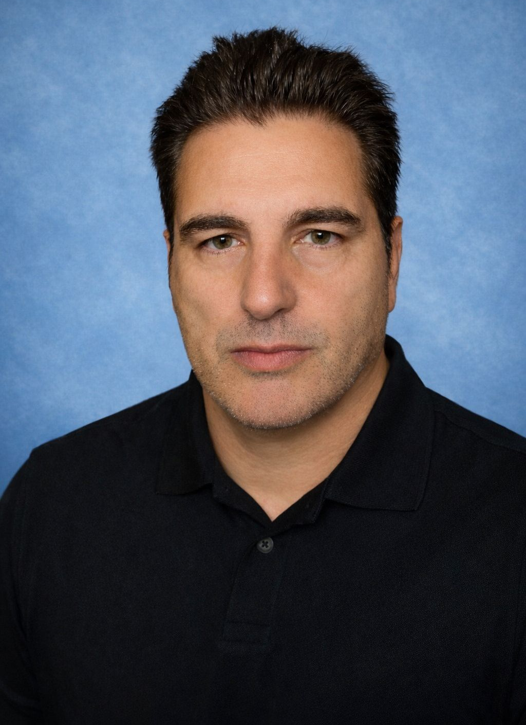 Man in black shirt, serious expression, against a blue background.