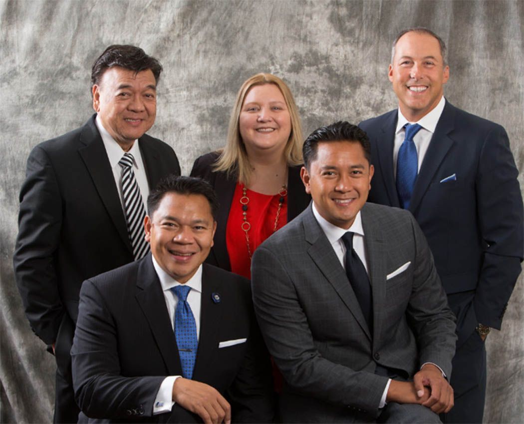 Five people in suits posing for a group photo against a gray backdrop.