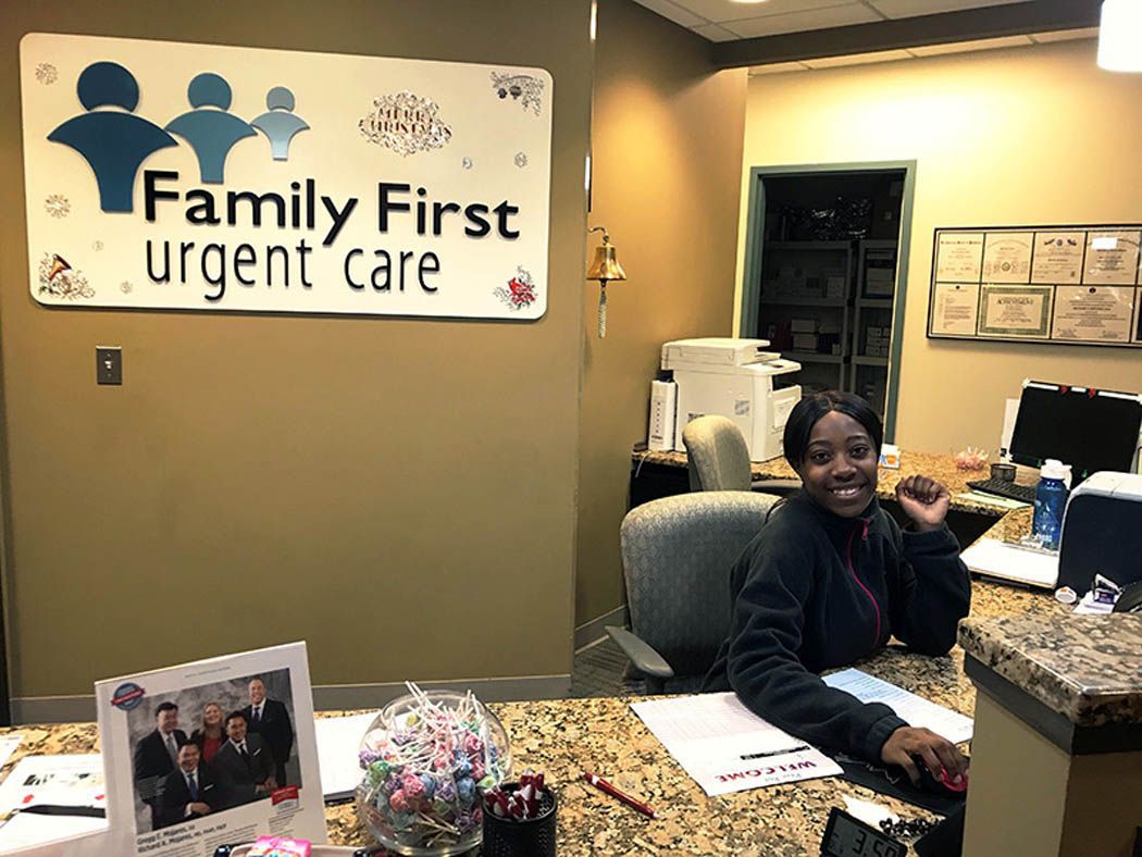 A person smiles while sitting at the reception desk of a Family First Urgent Care.