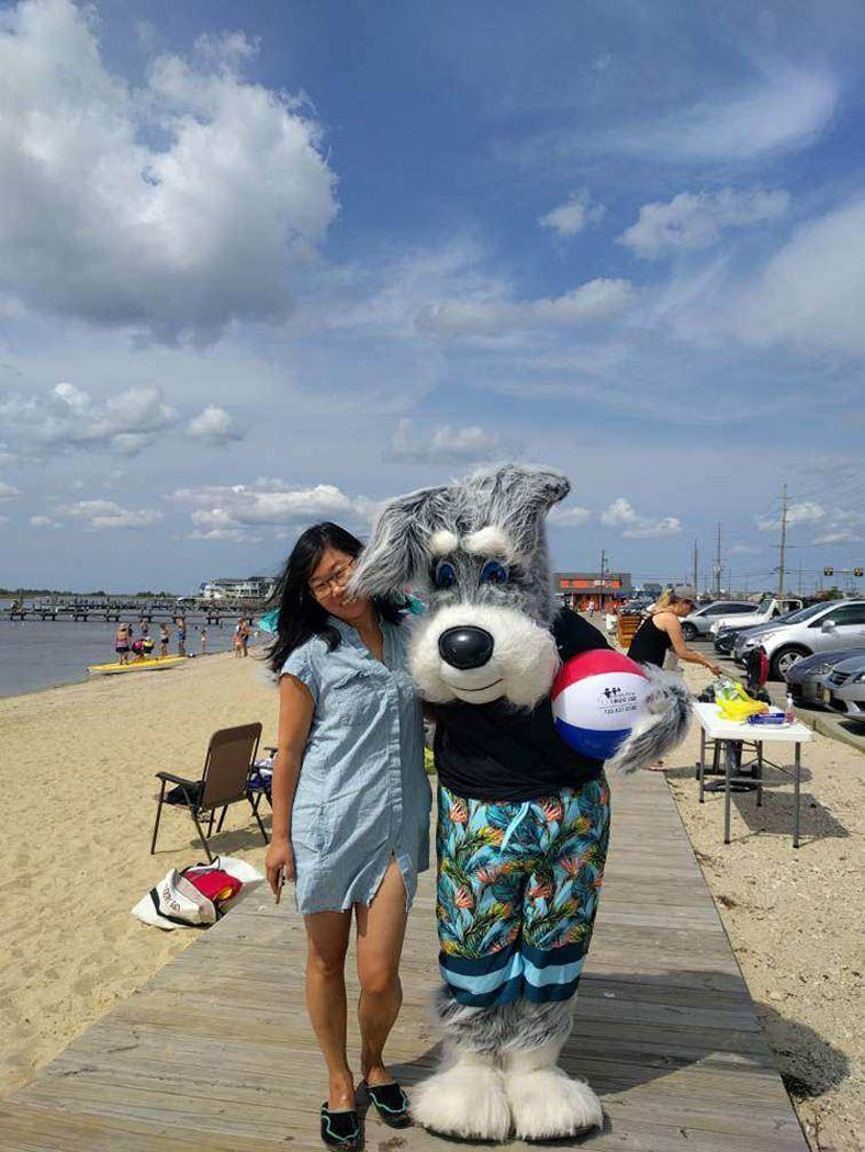 Woman in blue dress poses with dog mascot holding a beach ball on a boardwalk at the beach.