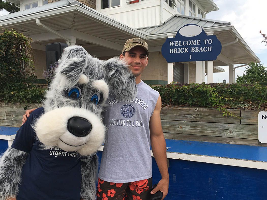 Man with dog mascot posing in front of a building; sign reads 