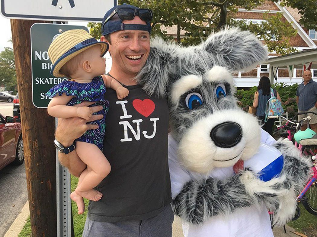 Man holding baby and posing with a dog mascot; man wearing an 