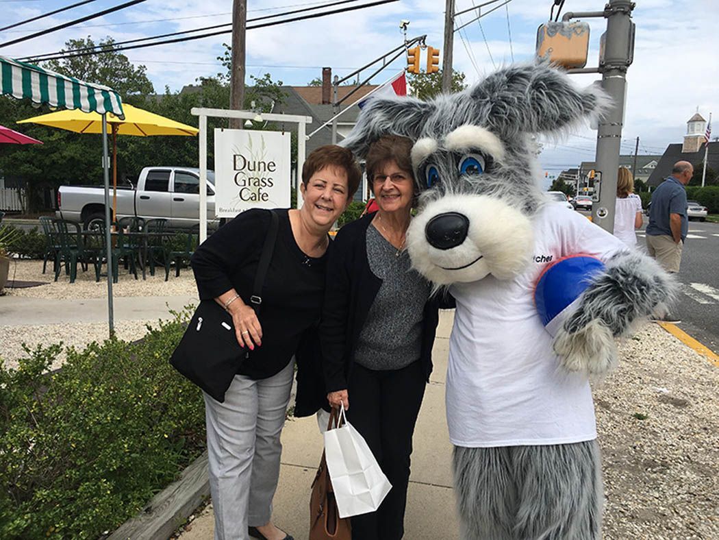 Two women pose with a dog mascot on a sidewalk outside a restaurant.