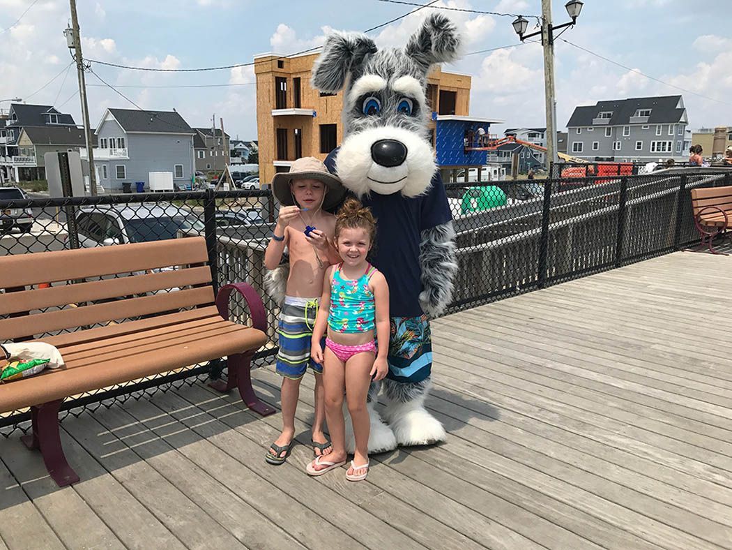 Two children pose with a dog mascot on a boardwalk.