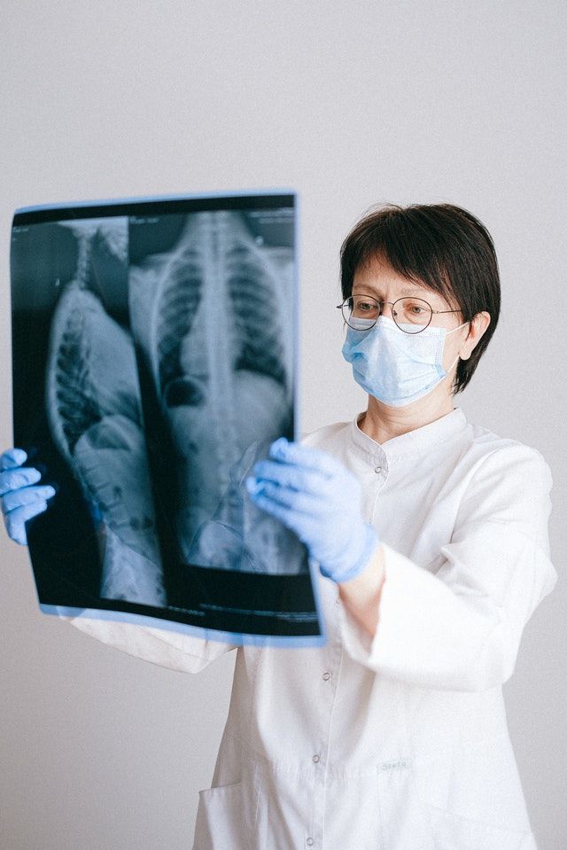 Doctor in white coat, blue gloves, and mask examining a patient's X-ray.