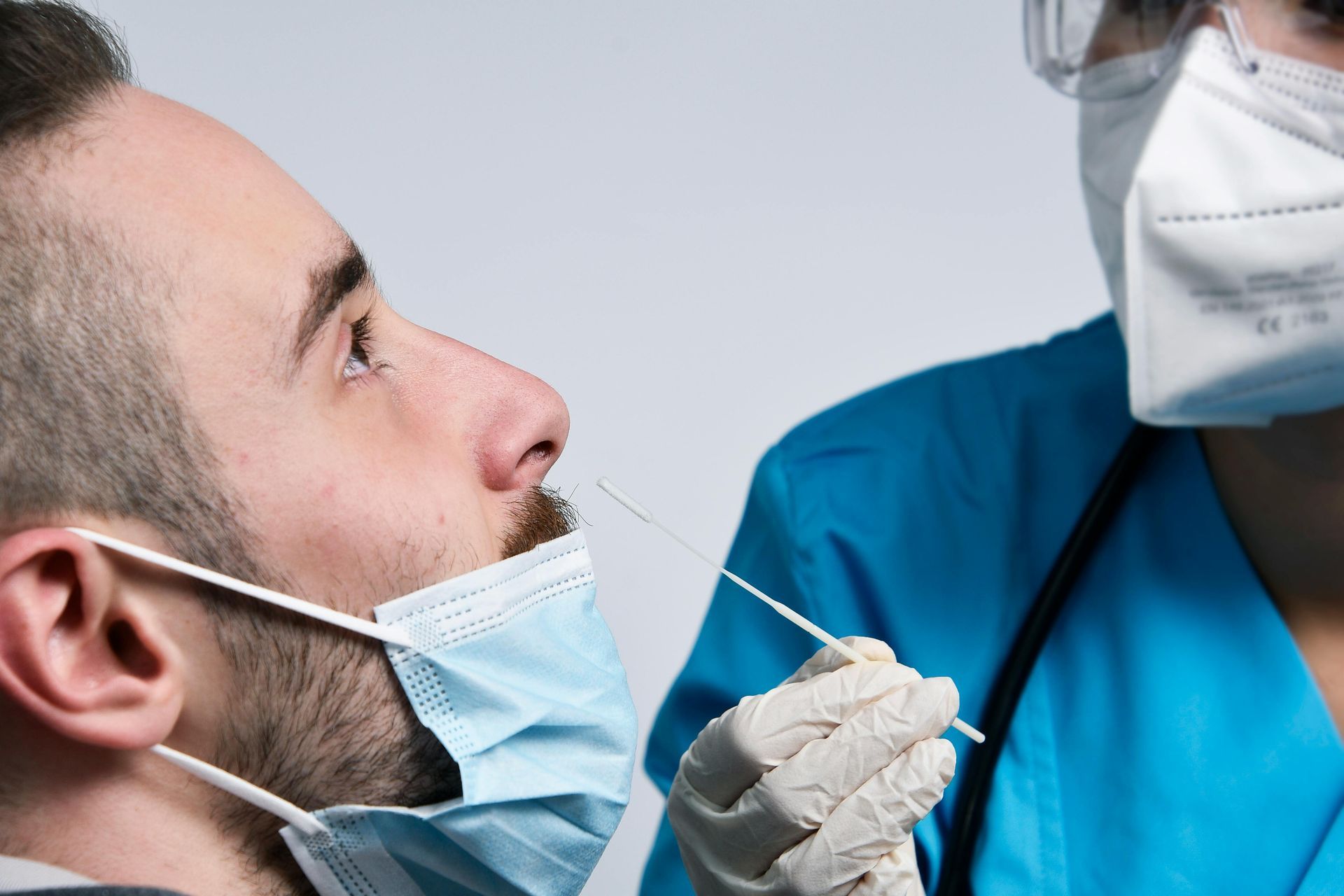 Dentist wearing mask swabbing a patient's nose with a test swab in a clinical setting