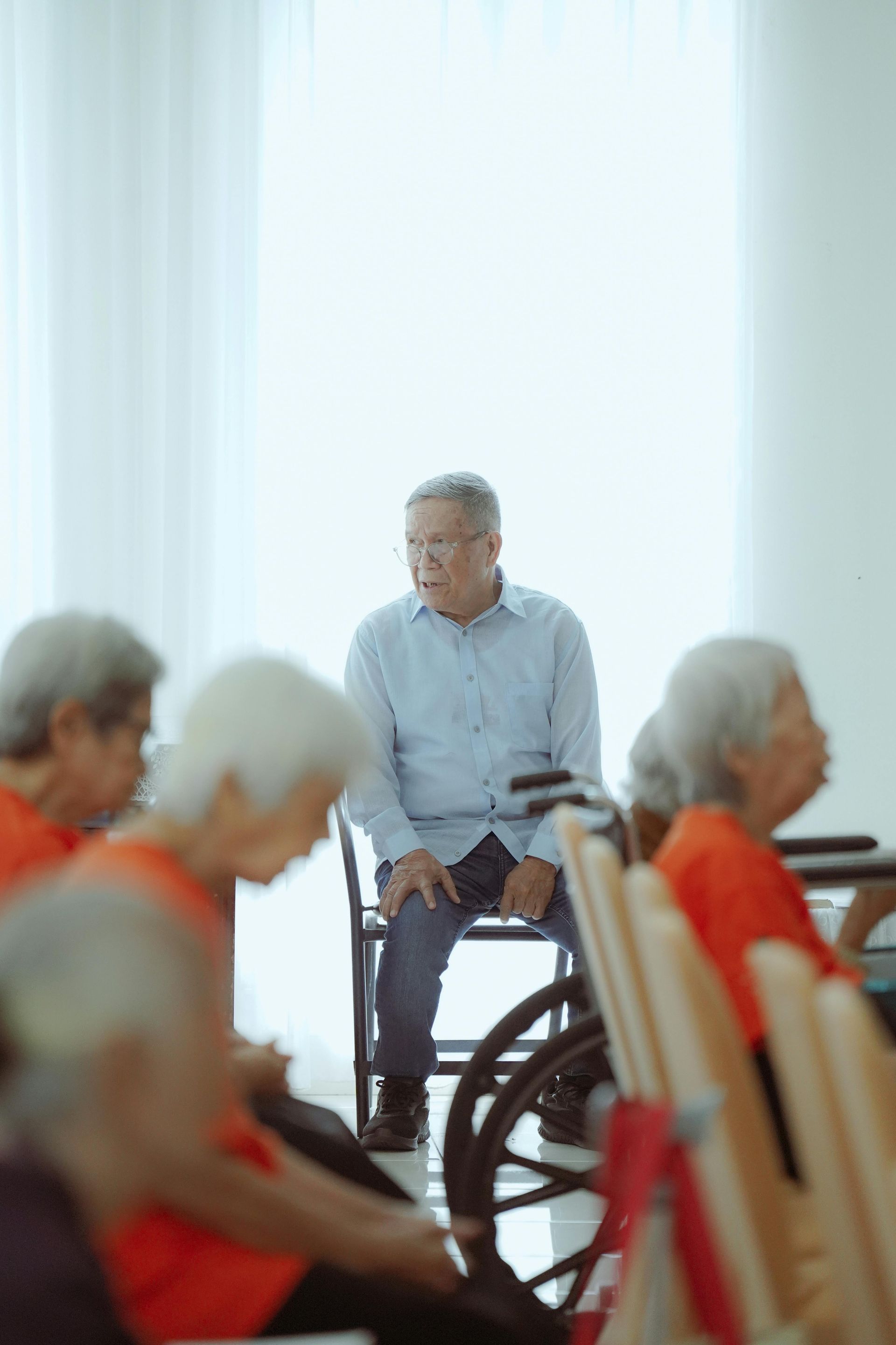 Man in a wheelchair seated among people in a bright care facility room