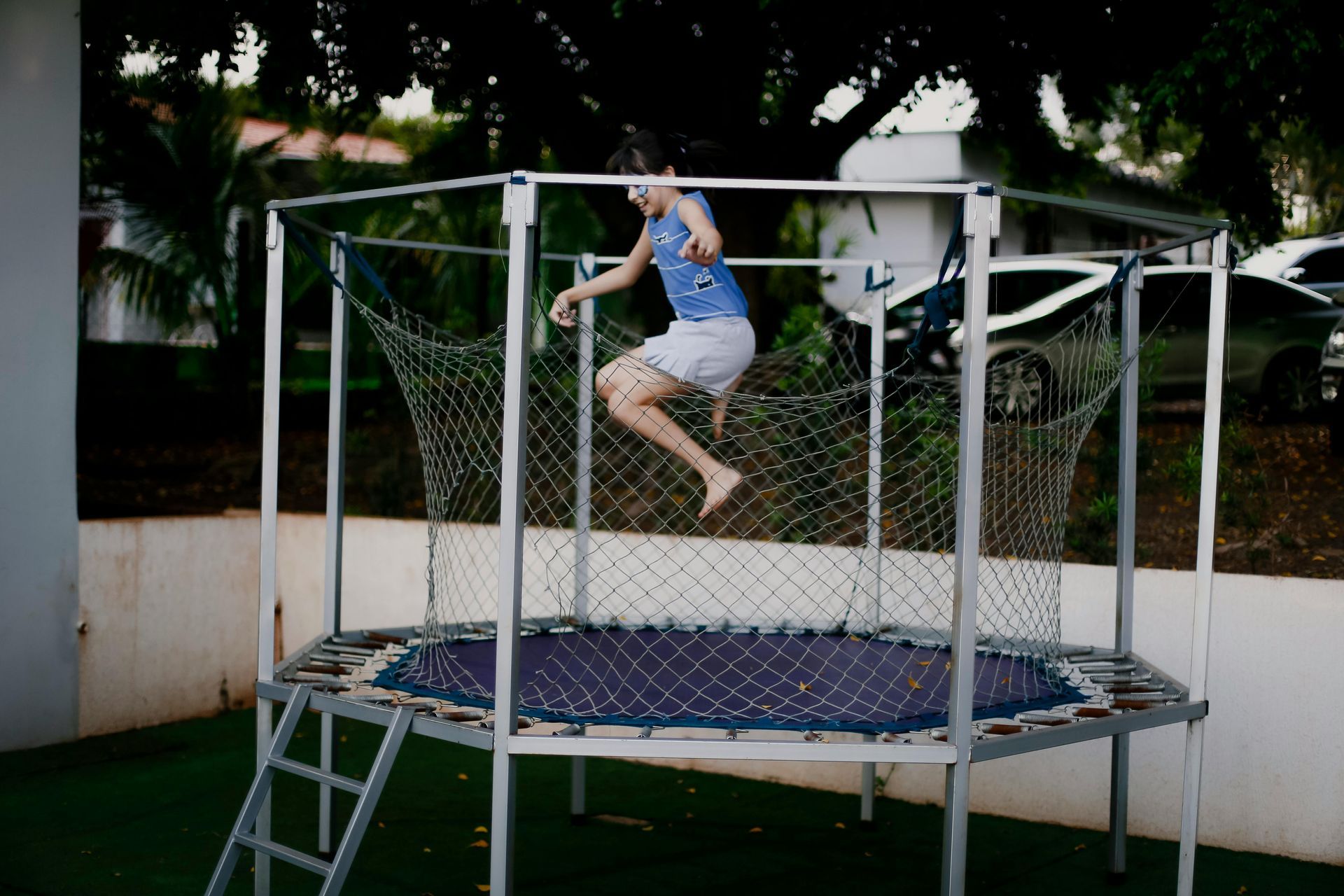 Child jumping on a trampoline in a backyard surrounded by a metal safety enclosure