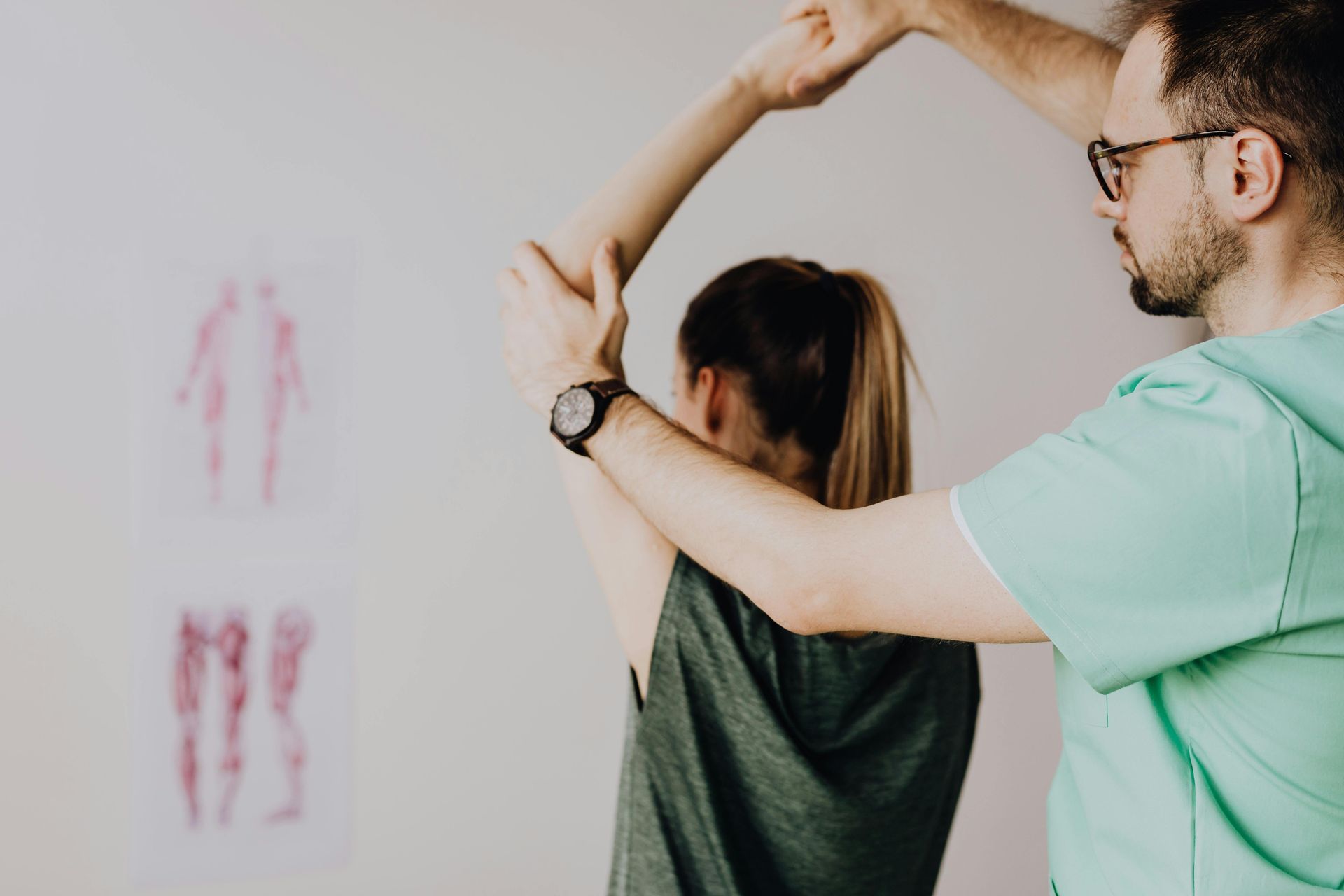 Physical therapist assisting a patient with an arm stretch in a clinic, with posture markings on the wall