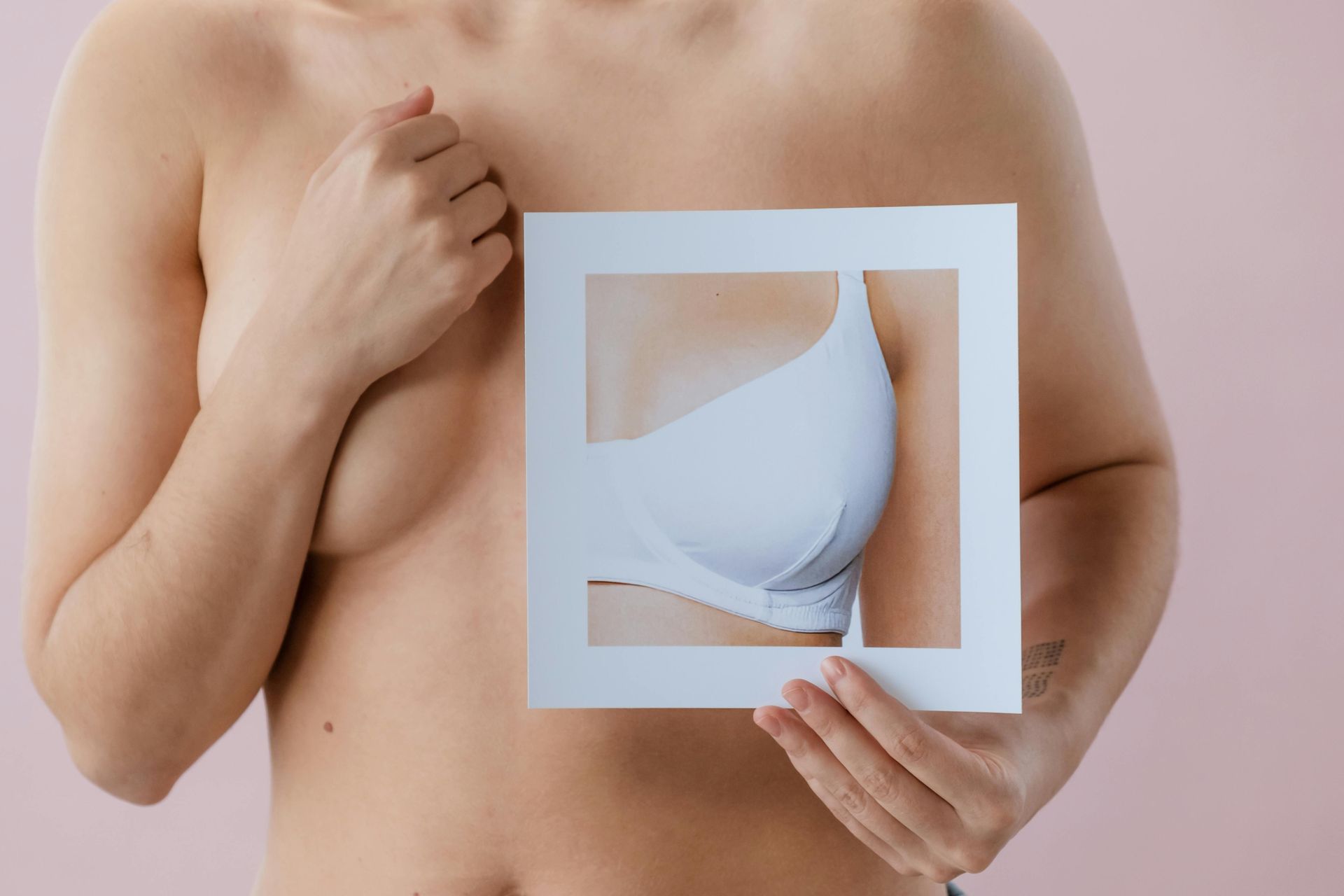 Person holding a cutout frame over their torso, revealing a breast implant illustration inside.