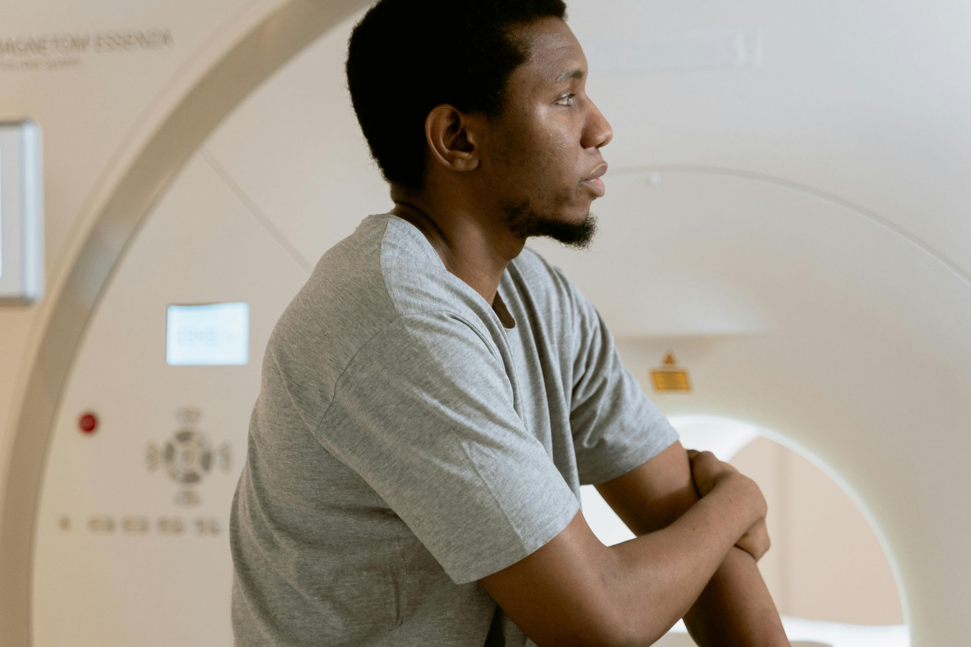 Person in a gray shirt leaning on a large white medical imaging scanner in a clinical setting.