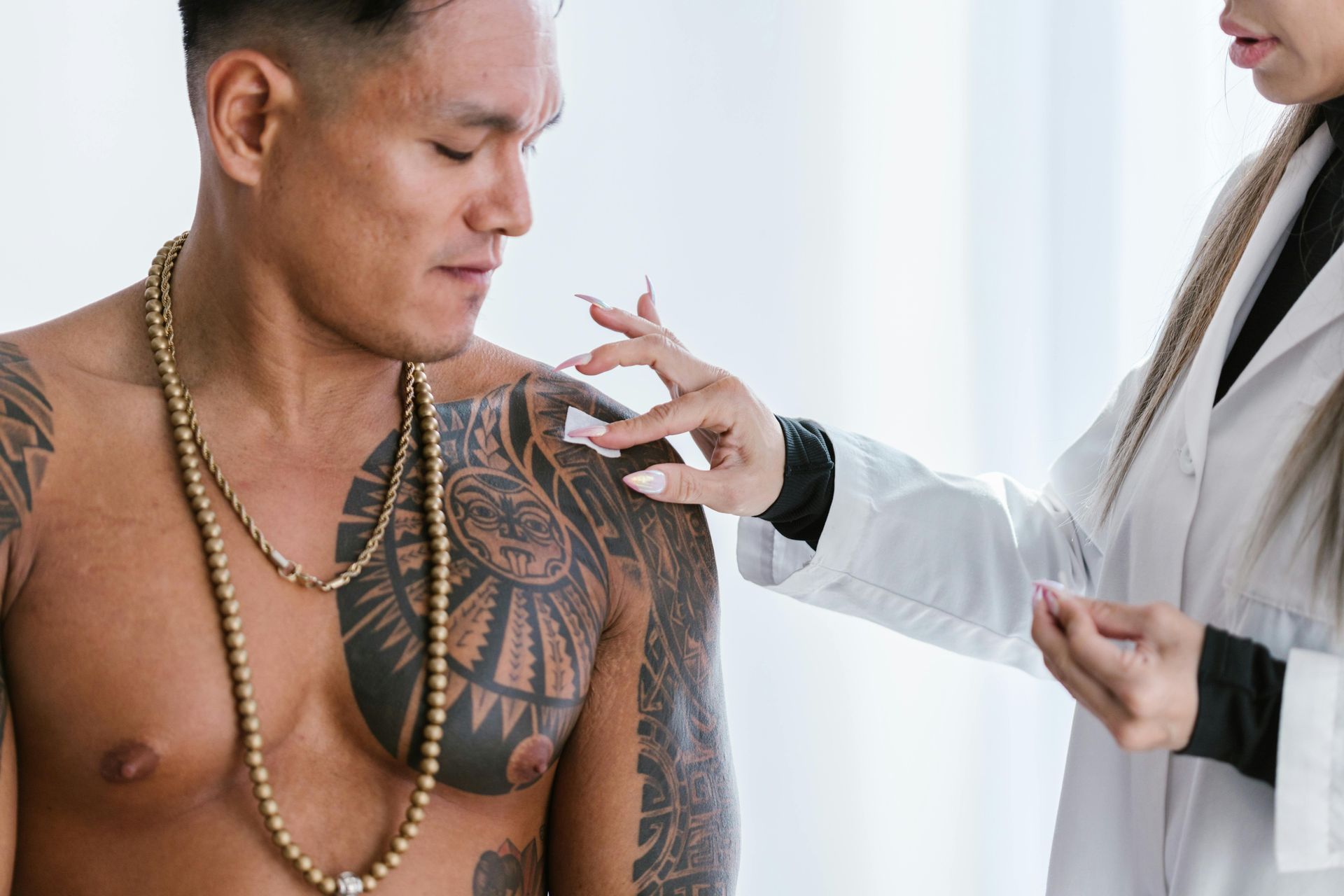 Health professional examining a man’s chest tattoo with a pen in a bright clinic setting.