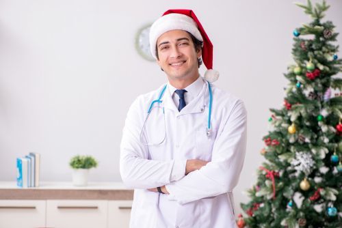 Doctor in Santa hat smiles in medical office with Christmas tree.