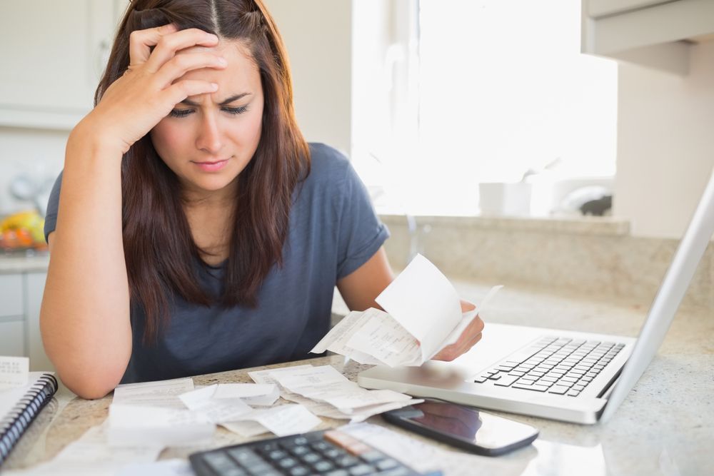Woman looking at bills with a worried expression, laptop and calculator nearby.