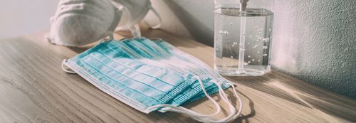 Face masks, hand sanitizer, and a spray bottle on a wooden surface, ready for use.