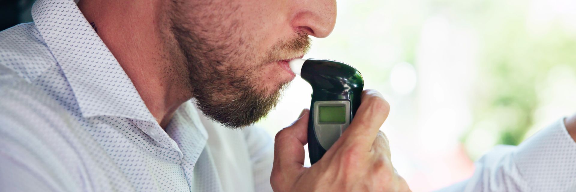 Man using a handheld breathalyzer, testing his breath indoors