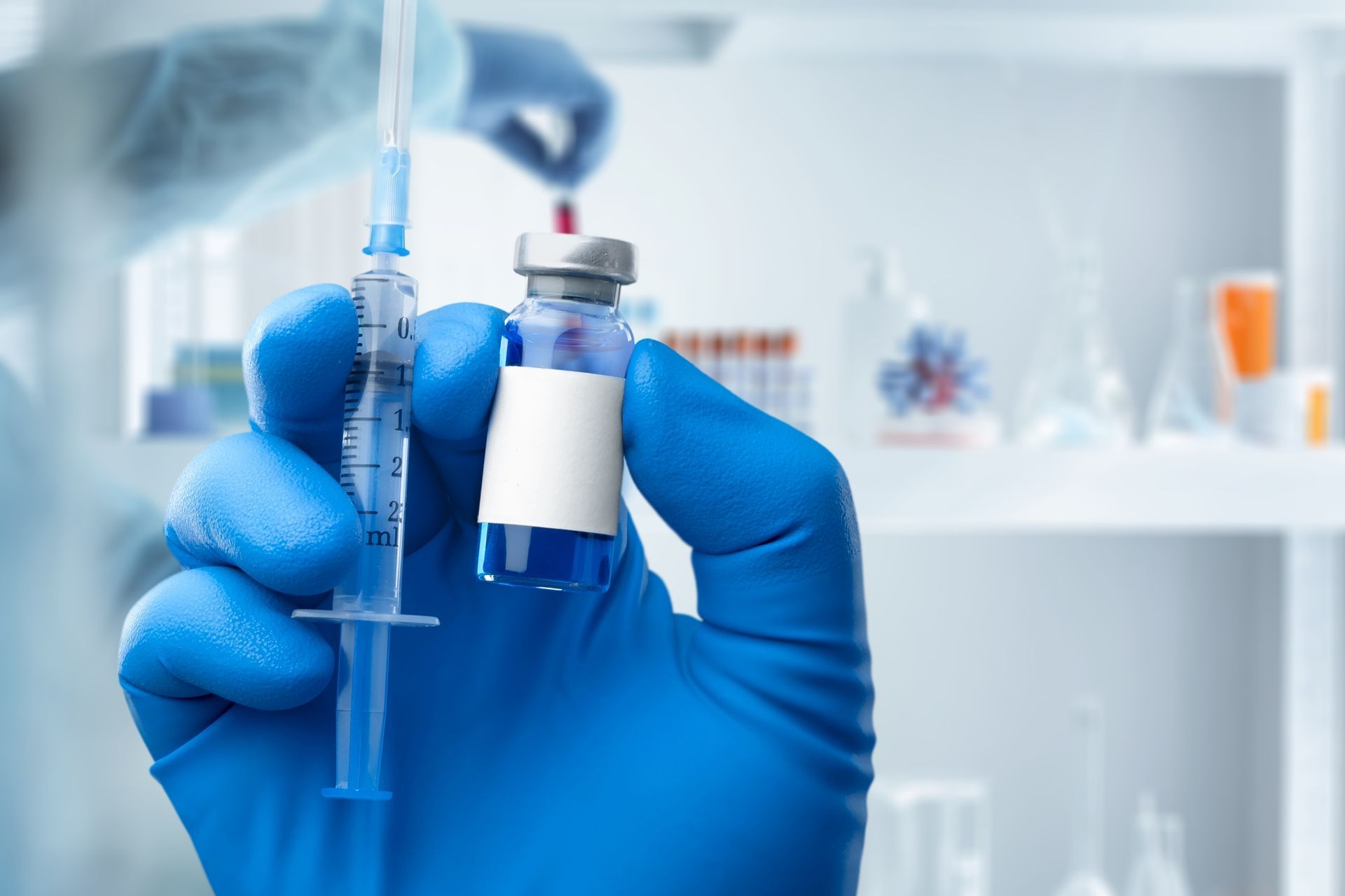 Blue-gloved hands holding a syringe and vaccine vial in a medical lab