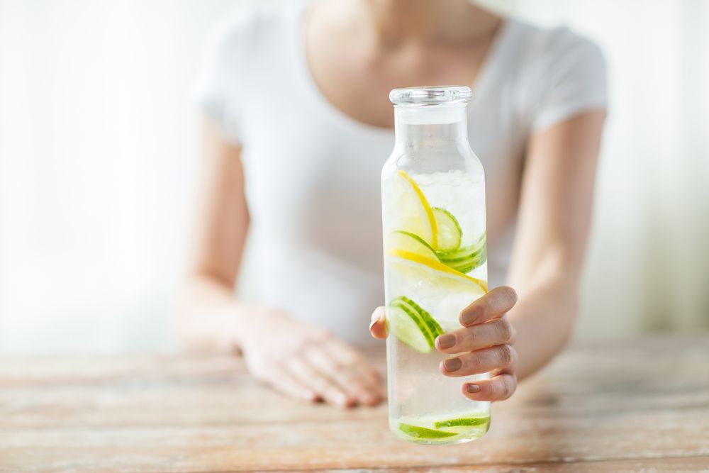 Woman holding a glass bottle of water infused with cucumber and lemon slices.