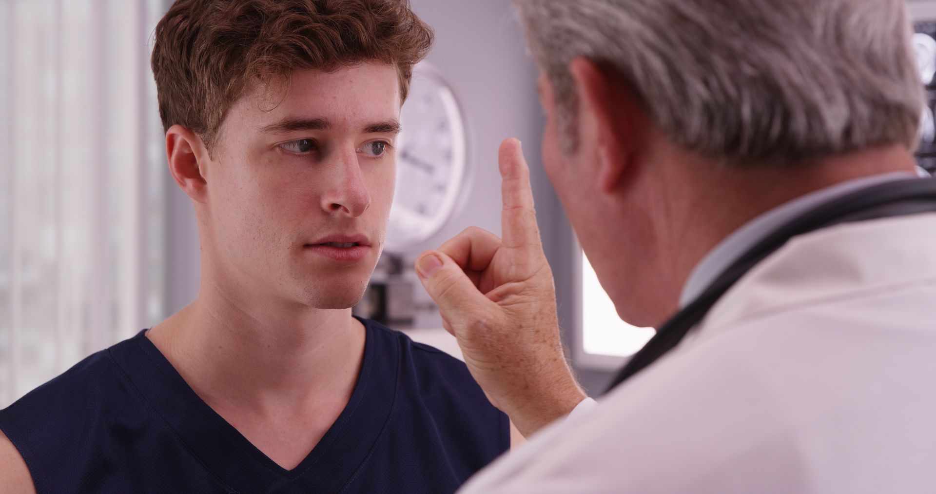 Doctor speaking to patient while pointing, in a bright clinic exam room.