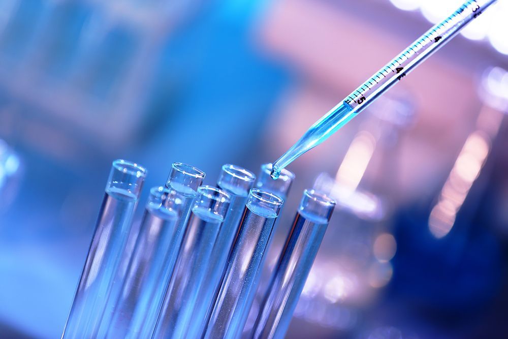 Test tubes with blue liquid being filled by a pipette in a lab setting.