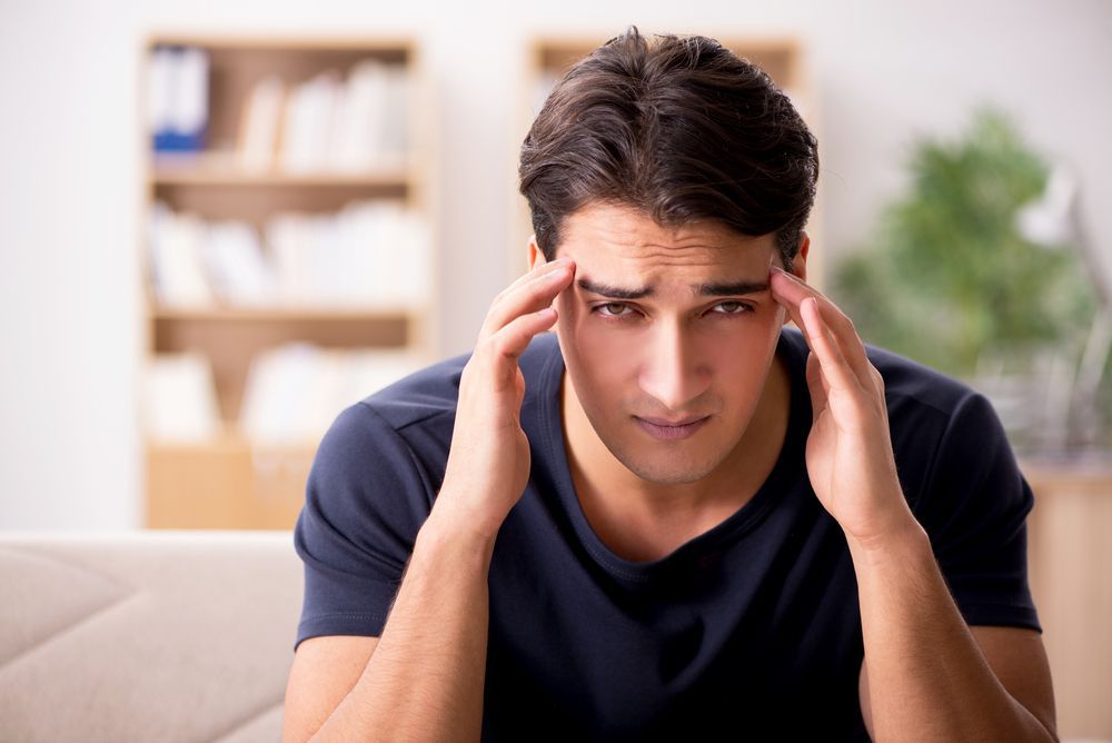 Man with hands on head, looking distressed, in an interior setting.