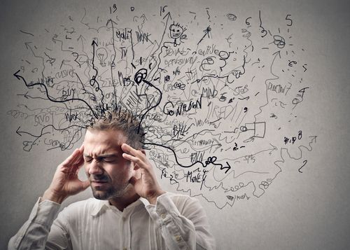 Man with hands on head, eyes closed, overwhelmed with scribbled thoughts emanating from his head.
