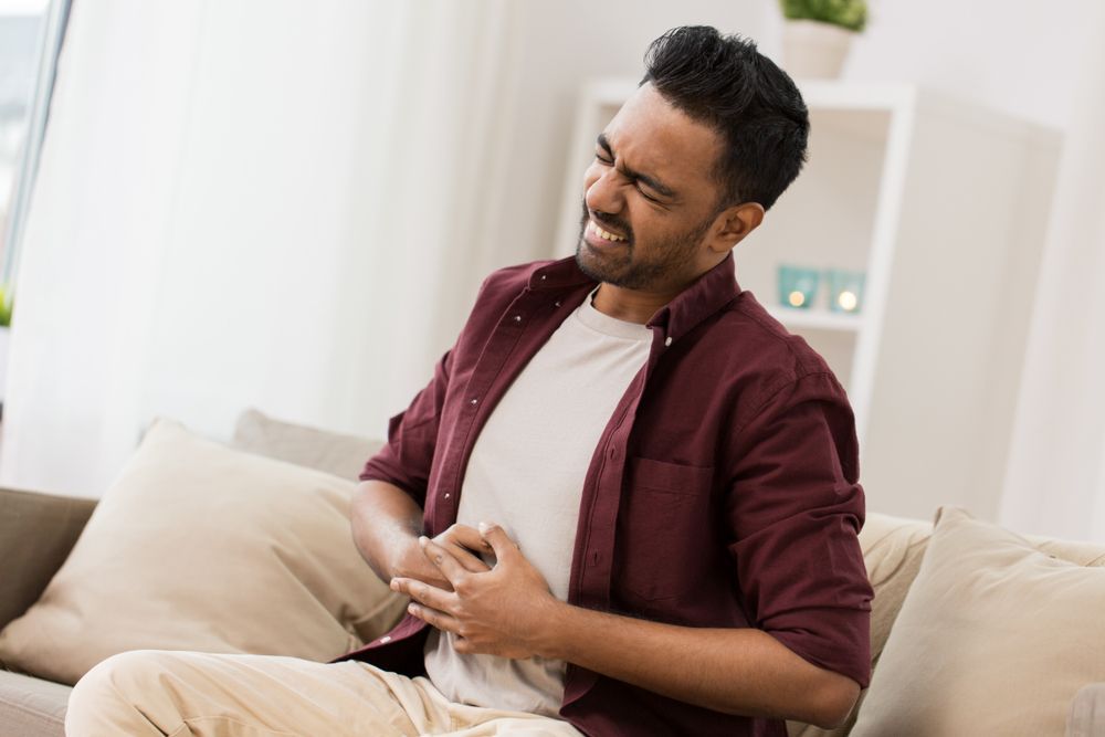 Man clutching his abdomen in pain while sitting on a couch.