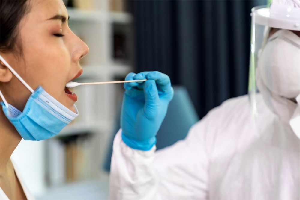 Healthcare worker swabbing a woman’s throat for a COVID-19 test while wearing PPE