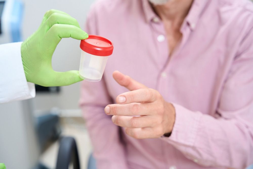 Gloved hand handing a urine sample cup to a person in a pink shirt