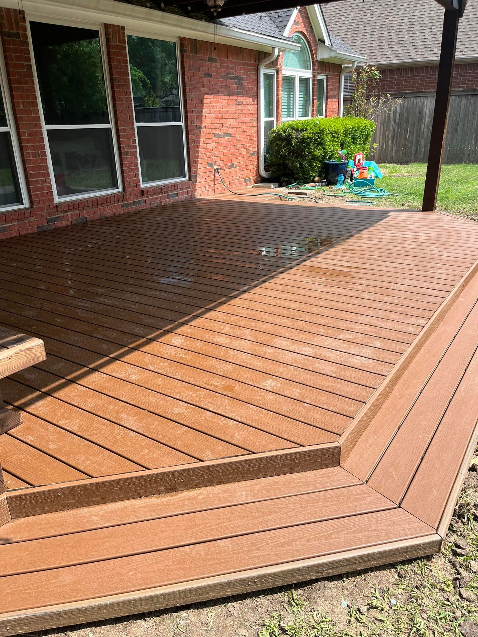 Wooden deck with curved steps and a brick house patio in the background