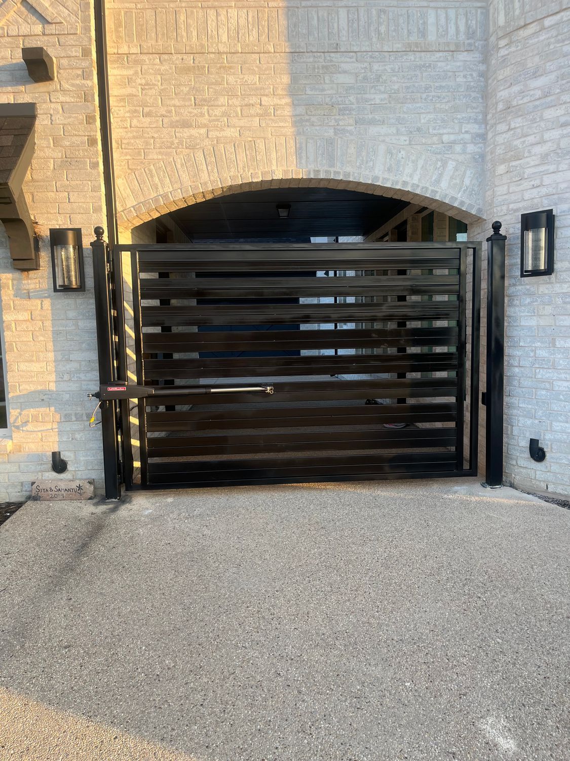 Closed black slatted gate in front of a stone archway and gravel driveway