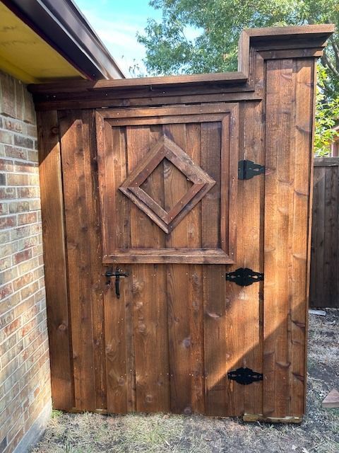 Rustic wooden gate with diamond carving beside a brick wall and yellow roof overhang.