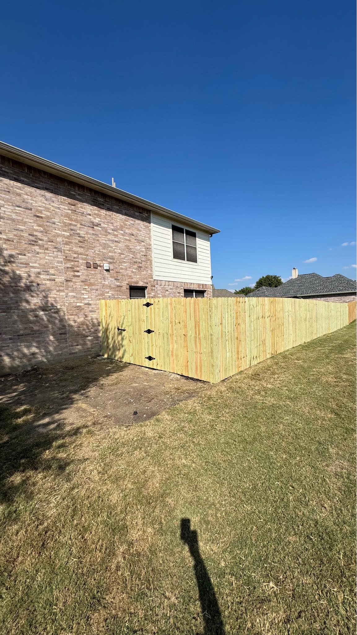 Brick house beside a new wooden fence in a sunny backyard under a clear blue sky