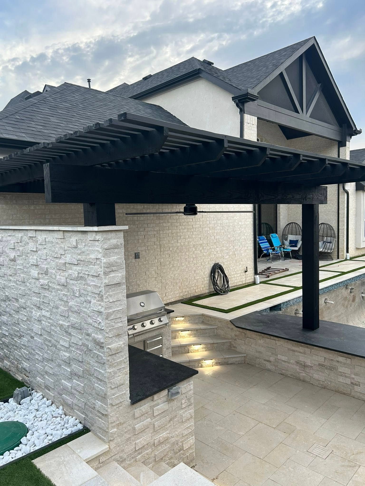 Modern house exterior with a black carport, stone wall, and paved driveway.