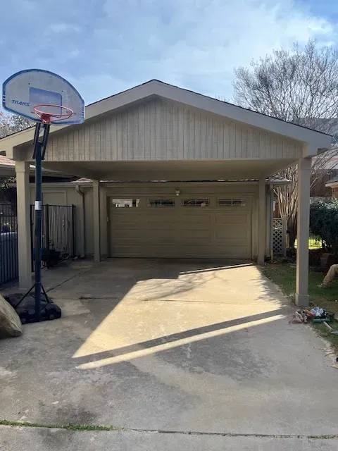 Driveway with a basketball hoop beside a beige garage on a sunny day.