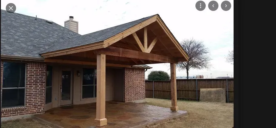 Brick house front porch with a gabled wooden roof and beige posts on a wet patio