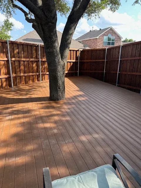 Backyard wooden deck with a large tree growing through the center and a patio chair in the foreground