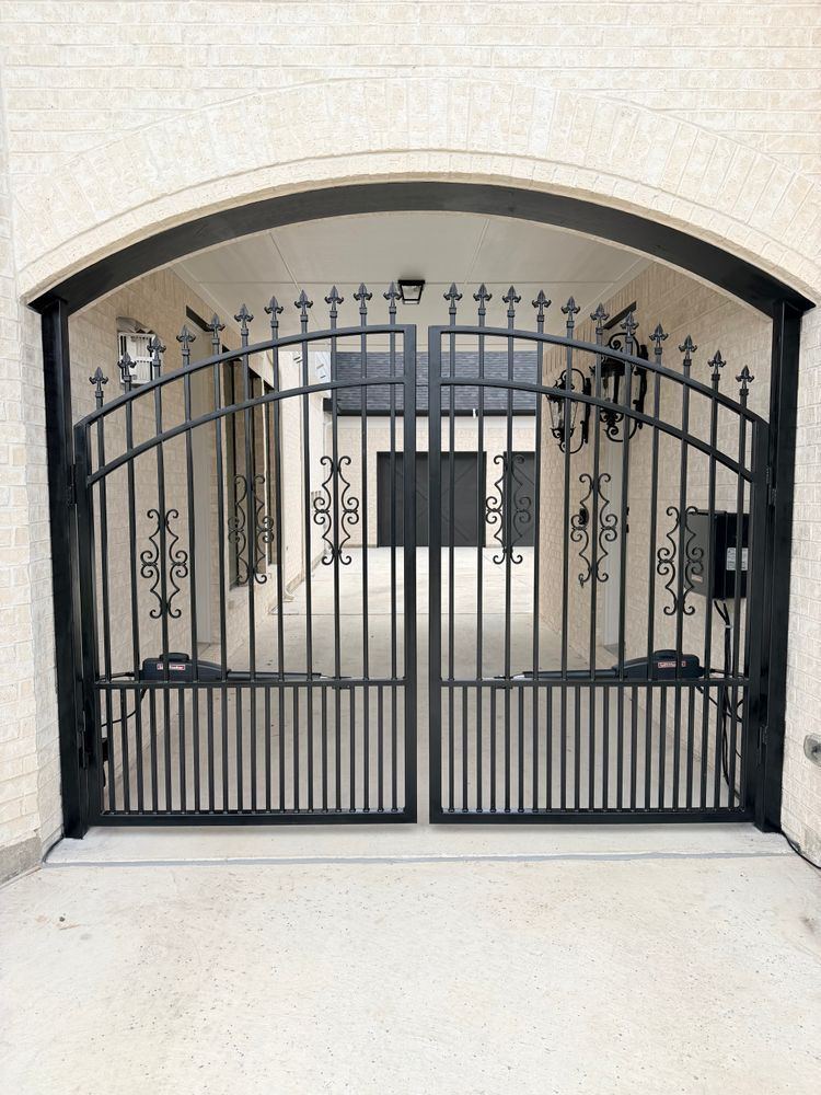 Black wrought-iron arched gate set in a light stone wall, with decorative scrollwork and vertical bars