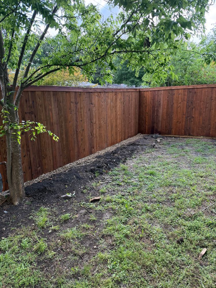 Backyard with a wooden fence, muddy grass, and a tree overhanging the left side.