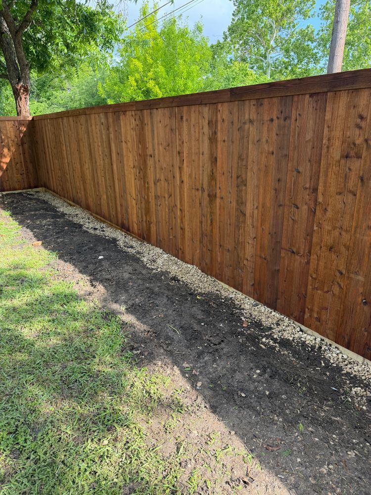 Wooden privacy fence along a grassy yard with a dirt strip at its base.