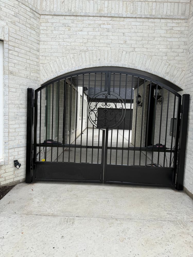 Black wrought-iron gate under an arched stone entryway, blocking a driveway.