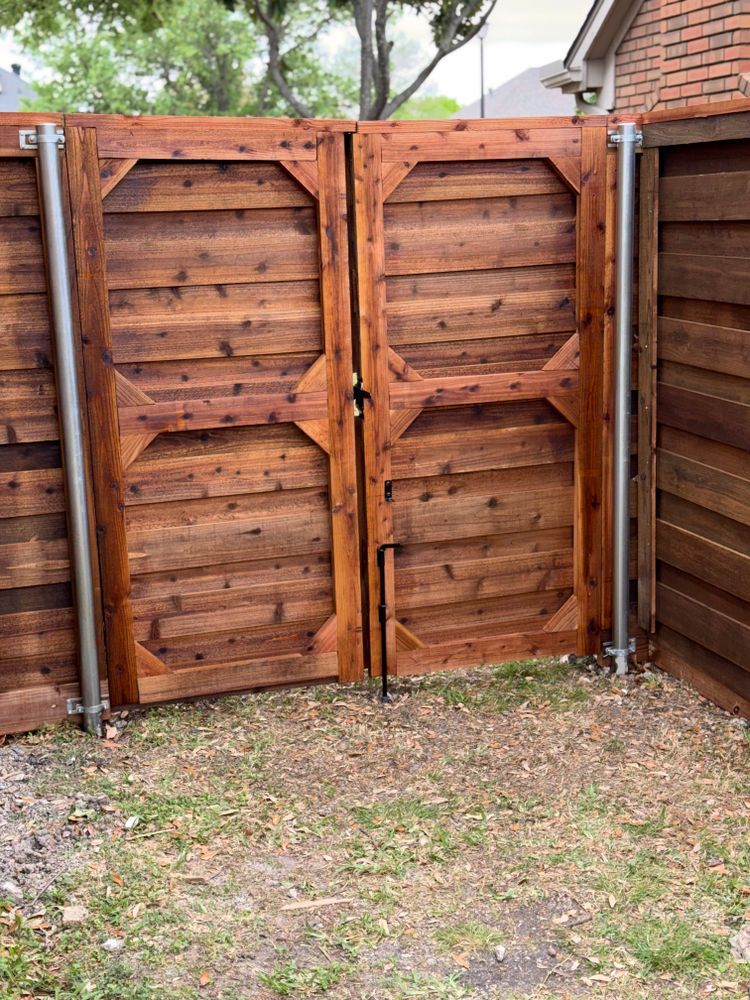 Wooden backyard gate with diagonal braces and a black latch, set in a fenced yard with grass and trees.