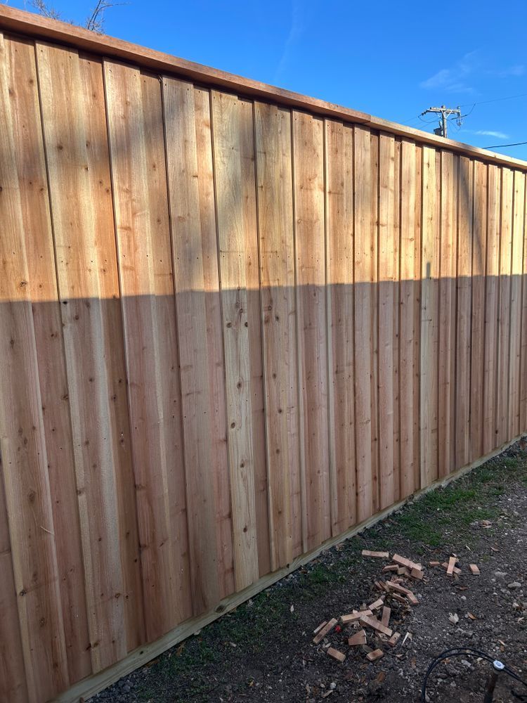 Wooden privacy fence with a sunlit top section and a shadowed lower section beside a dirt path.