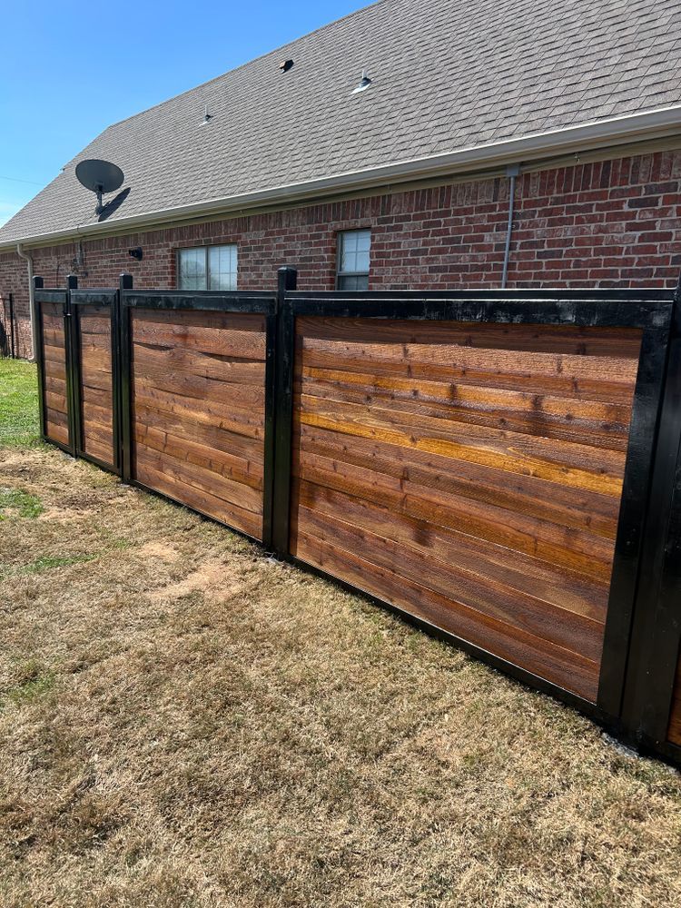 Backyard wood-and-metal privacy fence beside a brick house and dry grass lawn