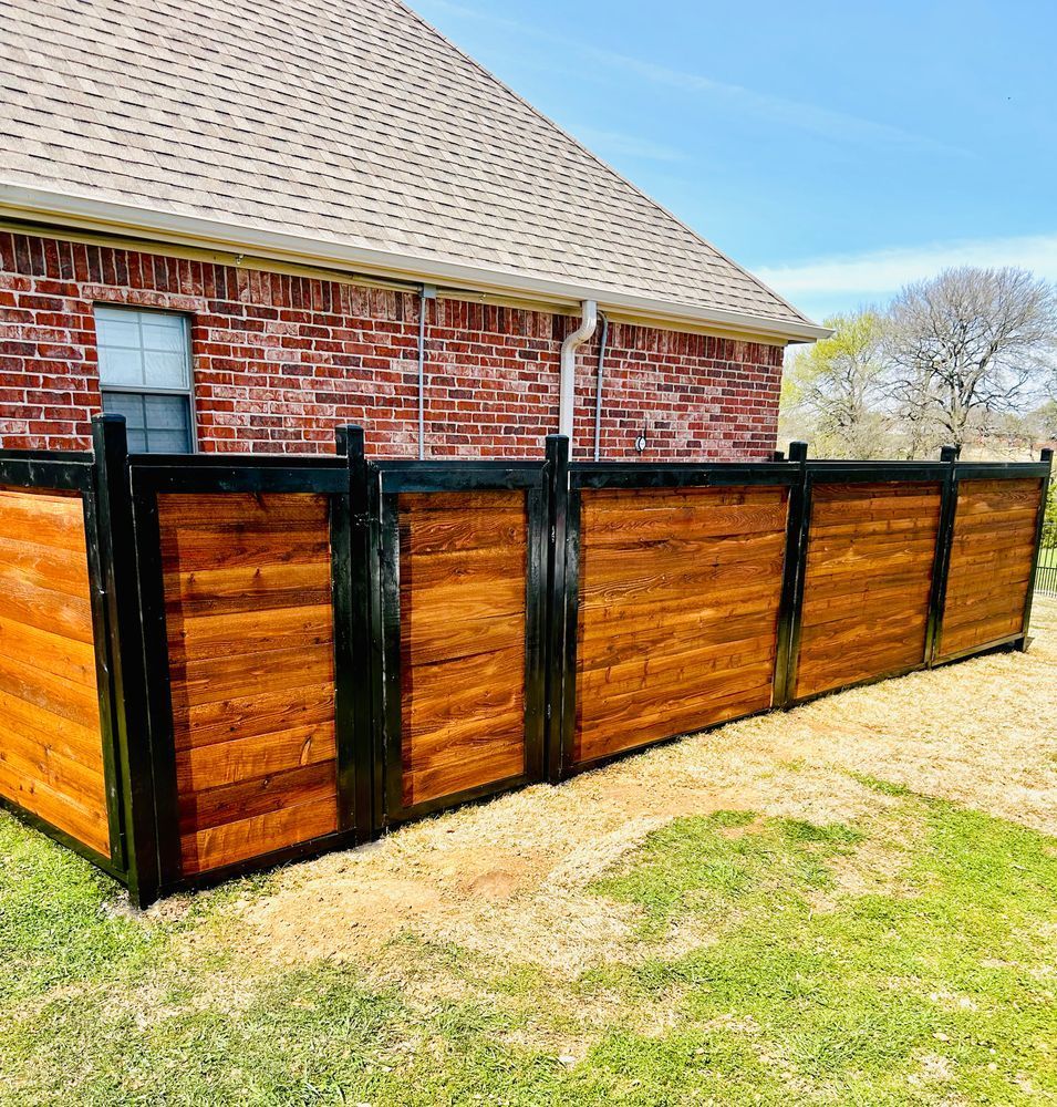 Wooden privacy fence with black posts beside a red brick house and grassy yard