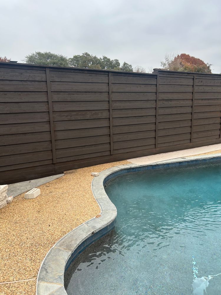 Backyard pool with curved edge, gravel border, and dark wooden privacy fence.