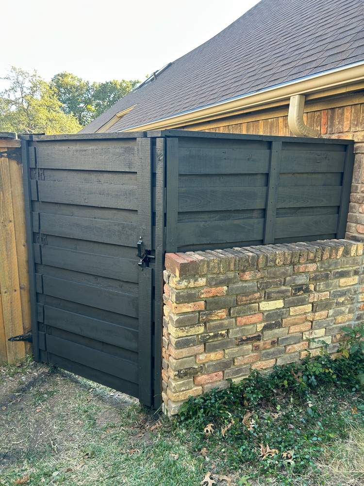 Black wooden gate beside a brick wall next to a house with a steep roof