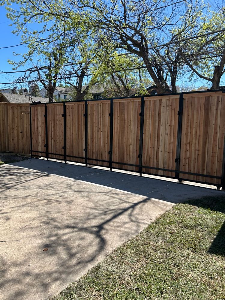 Wooden privacy fence beside a concrete driveway and patchy grass under leafless trees.