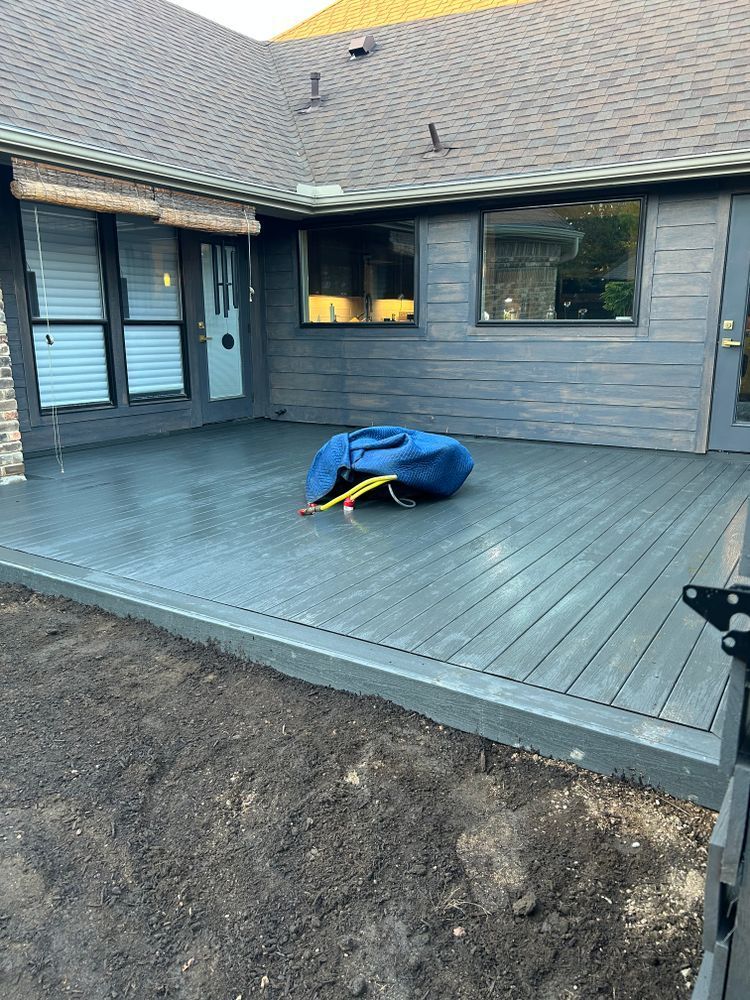 Back patio with gray decking, house siding and windows, and a blue tarp-covered item near the center