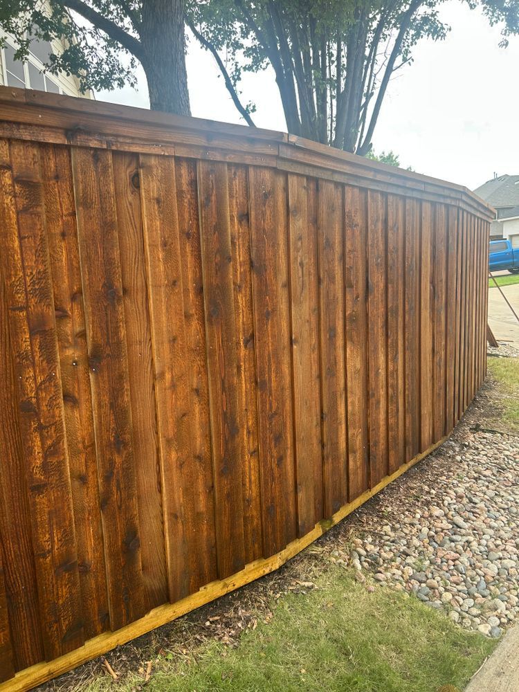 Wooden privacy fence along a gravel path, with trees and grass behind it.